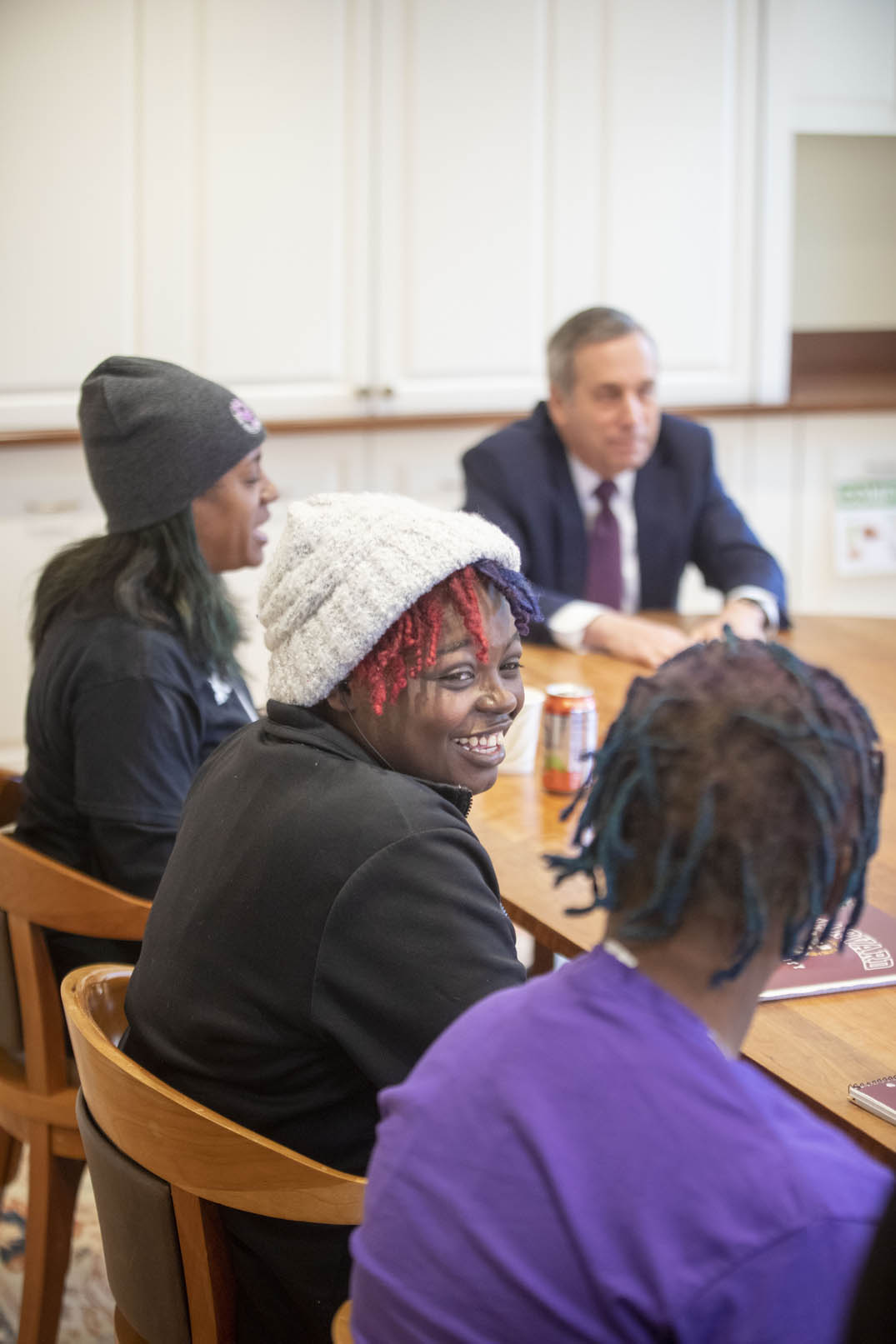 A group of students sit at a conference table with Larry Bacow.