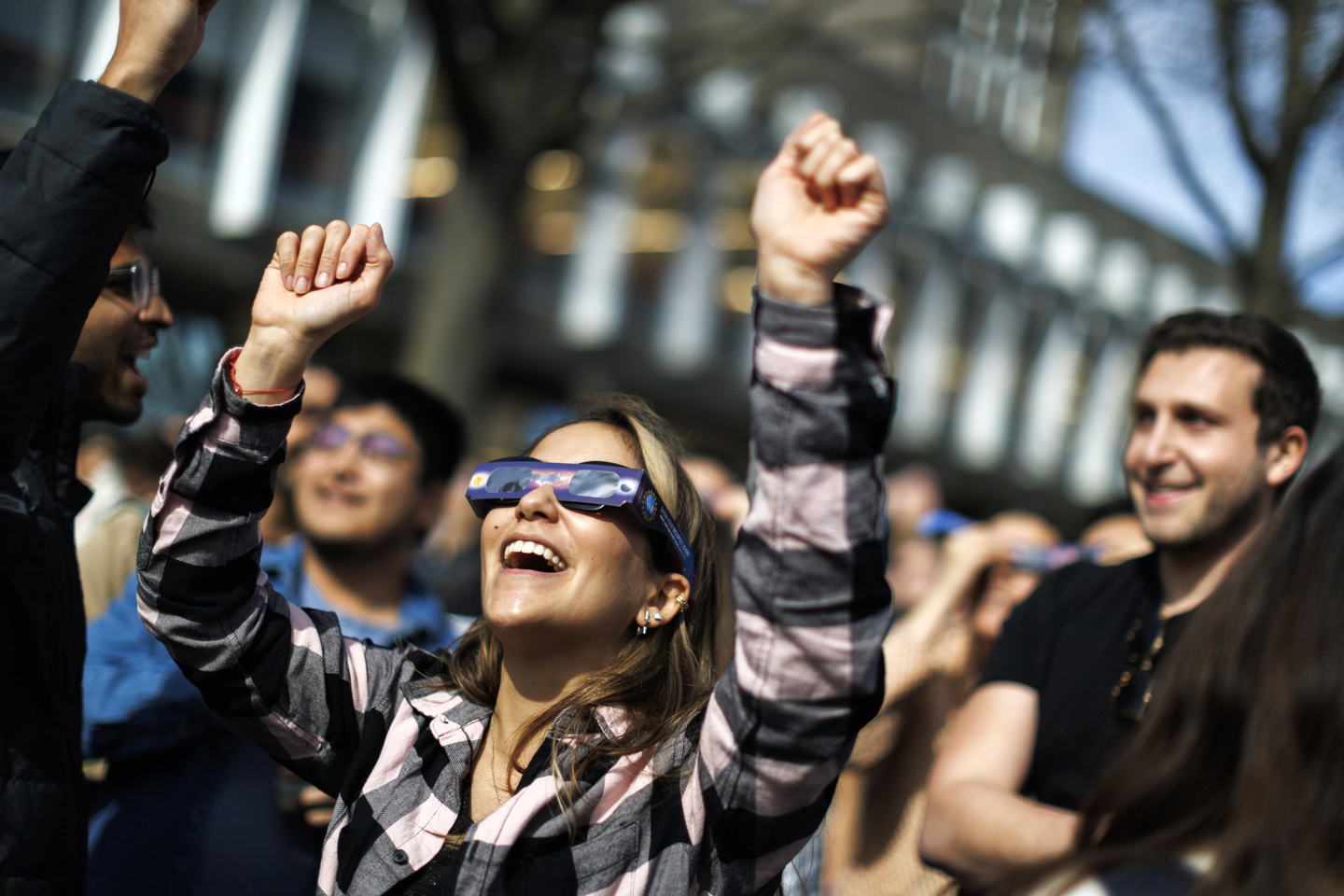 A woman wearing solar glasses raises her hands towards the sky.