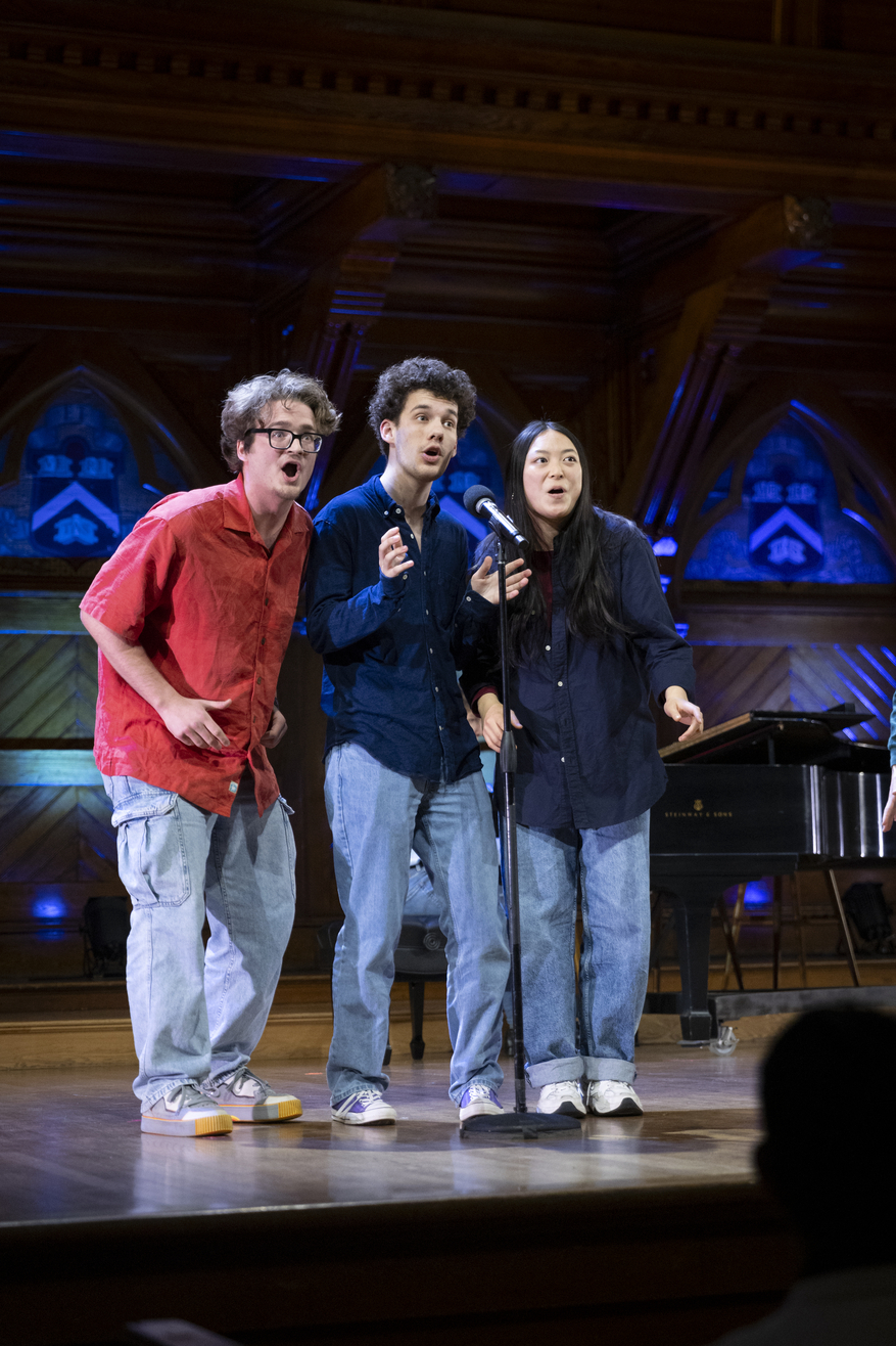 Three students in jeans looking surprised on stage.