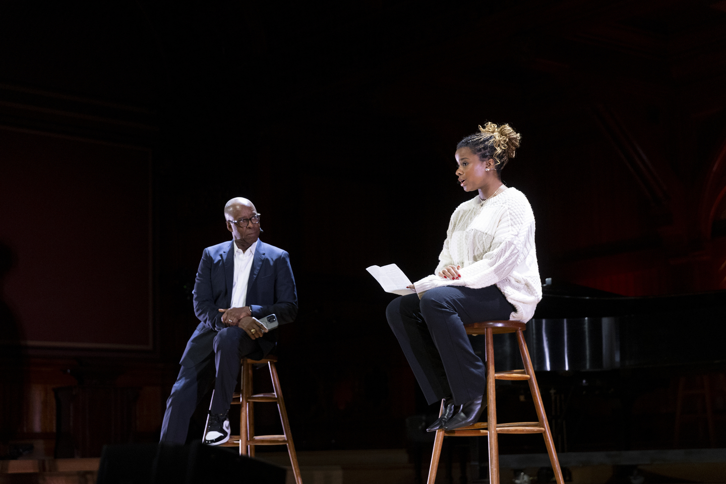 Two people on wooden stools speaking.