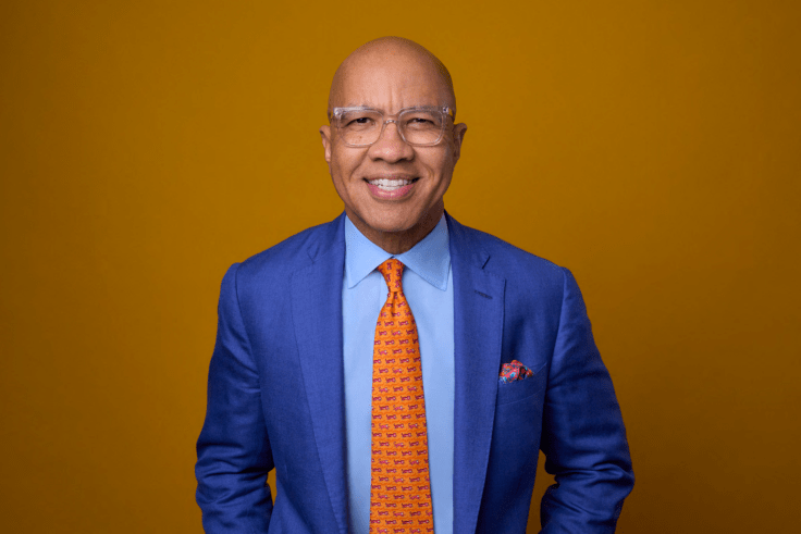 Man in a suit smiling with a yellow background.