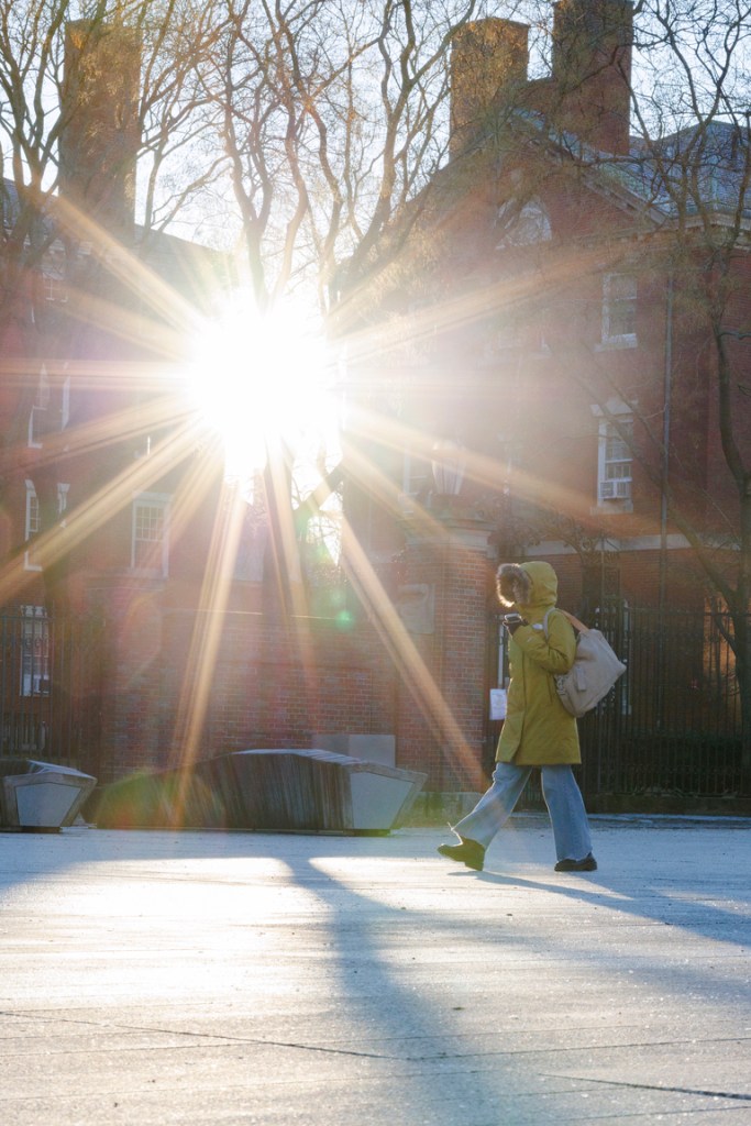 student walking across campus with a sunburst shining through two buildings.