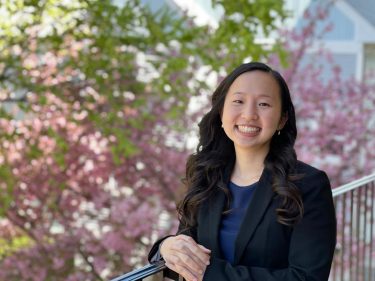 A woman stands outside near a pink flowering tree