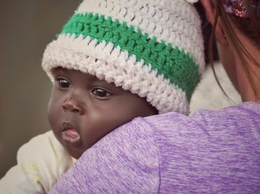 Small baby wearing a knit cap is held by a woman