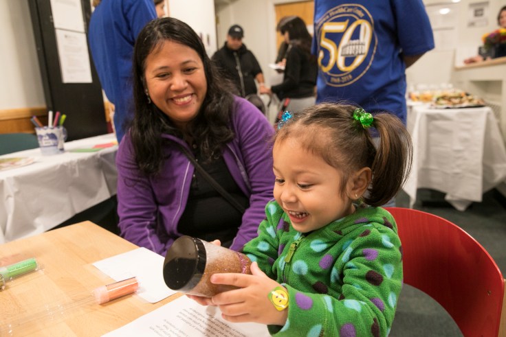 A mom looks on as her daughter holds a toy