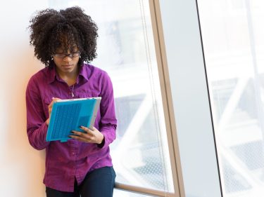 A woman takes notes while standing in an office near glass windows