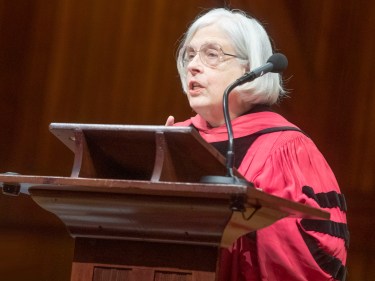 A woman wearing a red commencement robe speaks at a podium