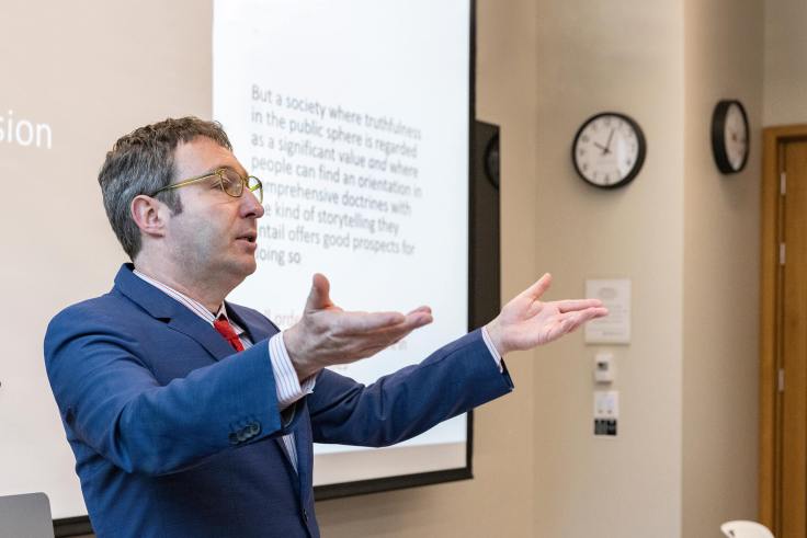 A man lectures in front of a smart board