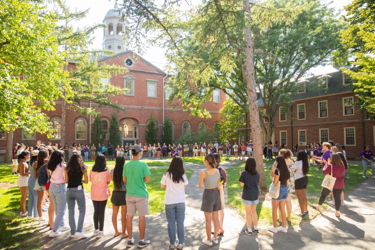 Students form a circle outdoors around a large lawn