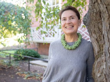 A smiling woman leans against a tree outside