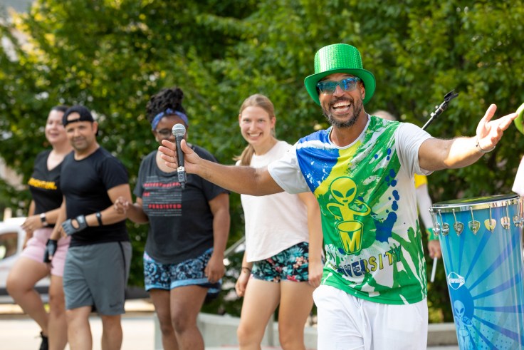 A singer holds out his arms wide while dancers smile behind him