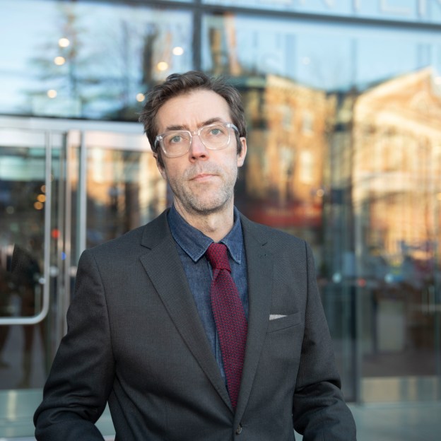 A man wearing a suit stands outside of a building with a glass entrance