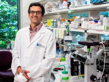 A scientist wearing a white coat stands in front of his lab