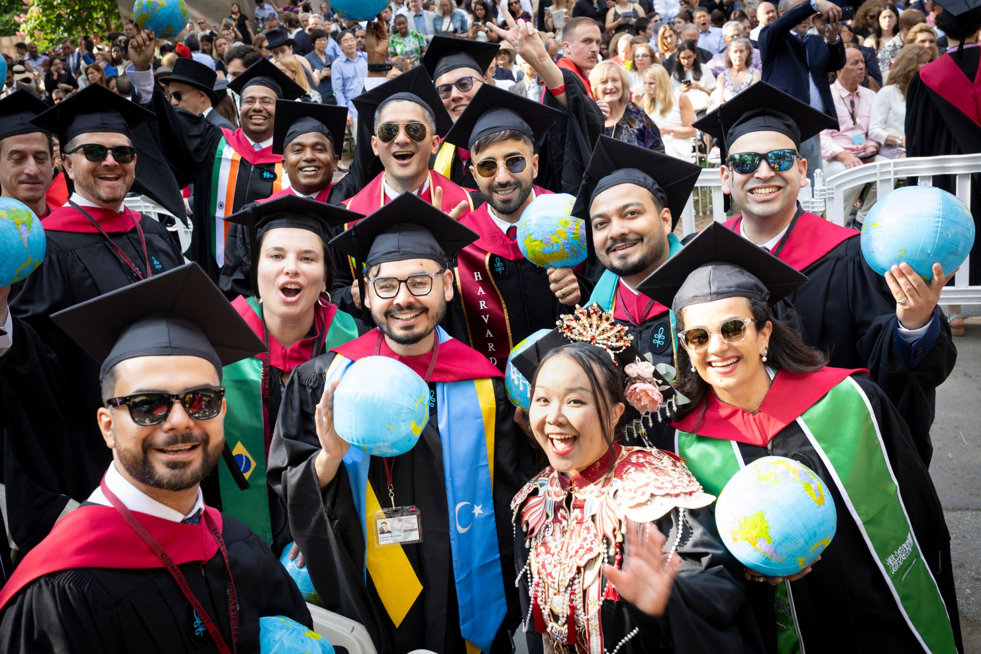 A large group of graduates from Harvard Kennedy School smile and pose holding inflatable globes