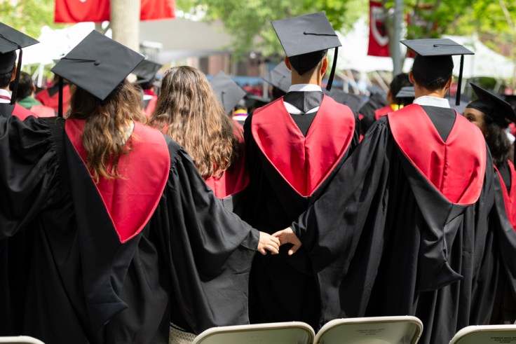 Two Harvard graduates holding hands behind the backs of two graduates