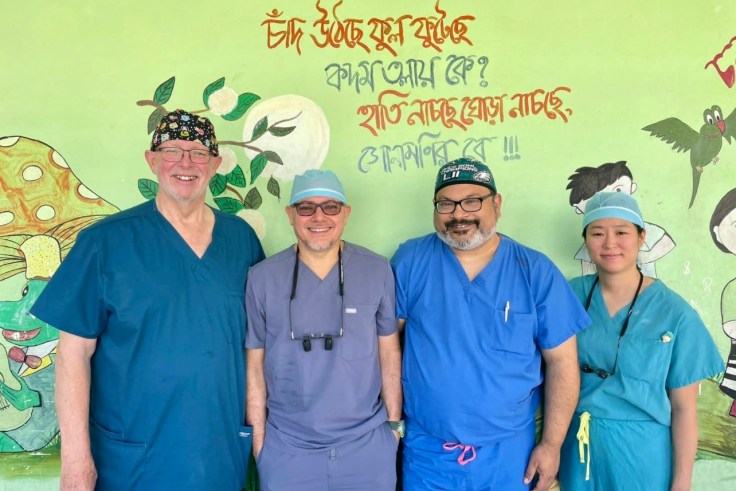 Four dental surgeons wearing scrubs stand against a bright green wall