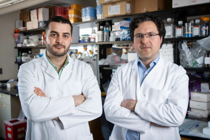 Two scientists wearing white coats pose together in a lab.