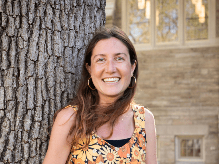 A woman leans against a tree for a headshot photo