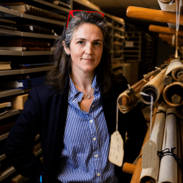 A woman stands in a room filled with maps of all different sizes