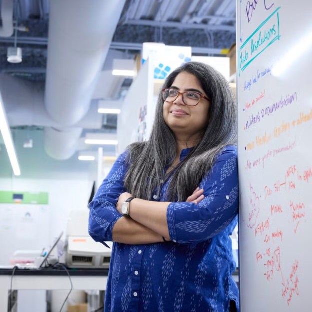 Smita Gopinath stands with her arms crossed in a lab by a whiteboard