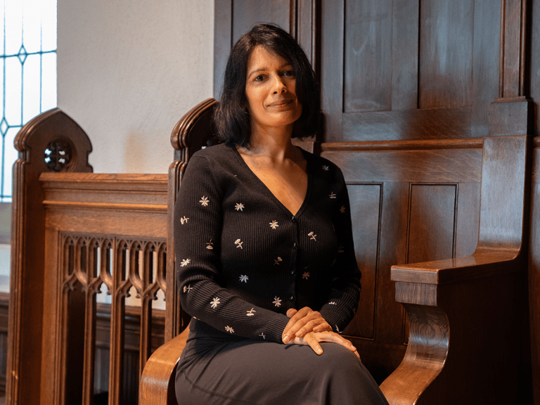 Sabbi Lall sits in a wodden pew.